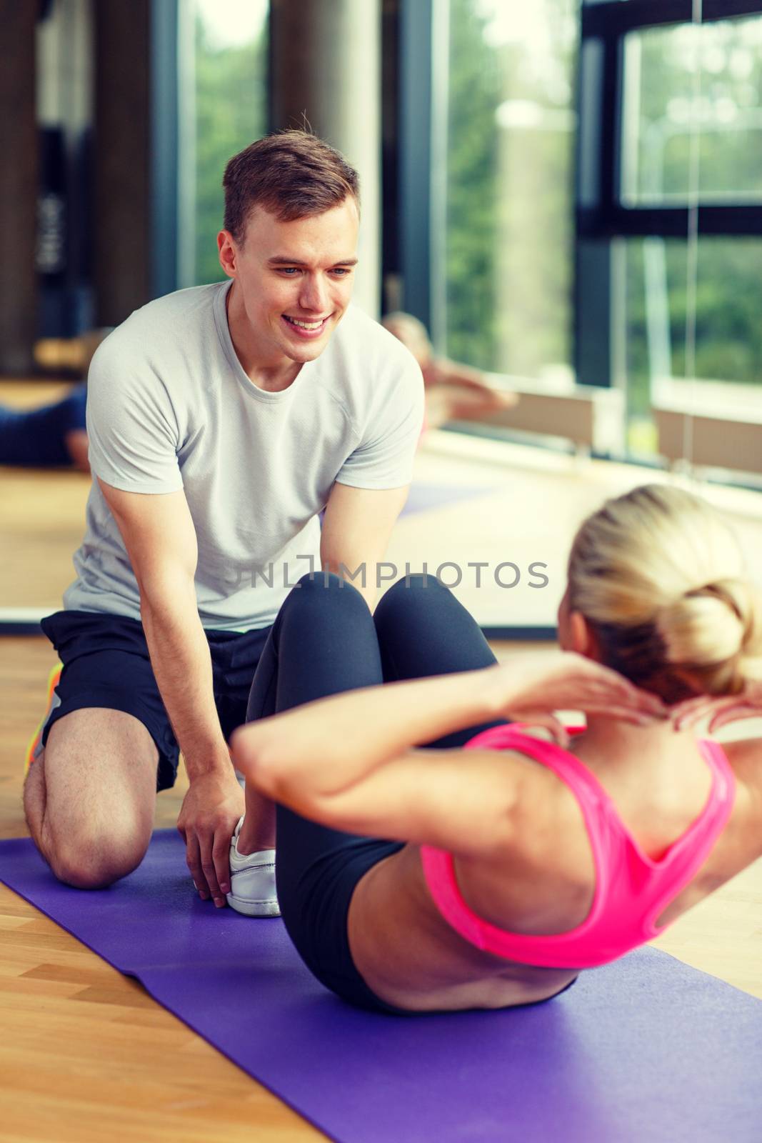 smiling woman with male trainer exercising in gym by dolgachov