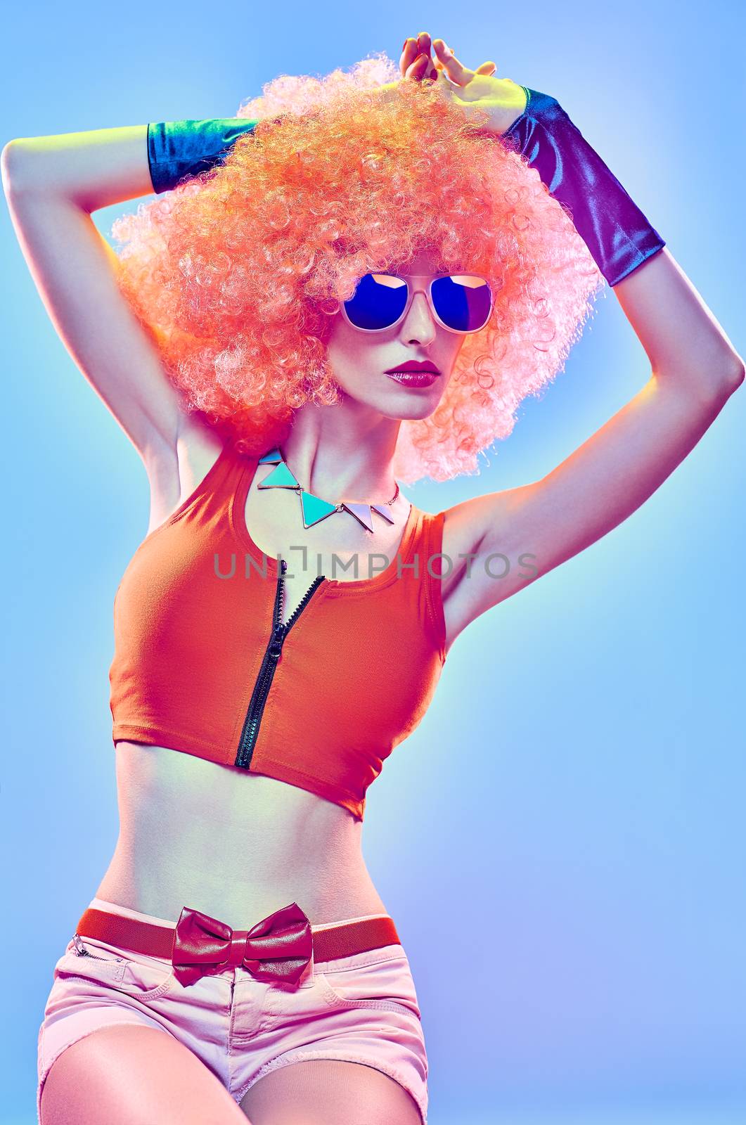 Fashion portrait of sexy beauty woman, unusual creative people. Vivid party provocative attractive girl in stylish sunglasses and gloves. Curly hipster girl, afro hairstyle on blue, copyspace, toned