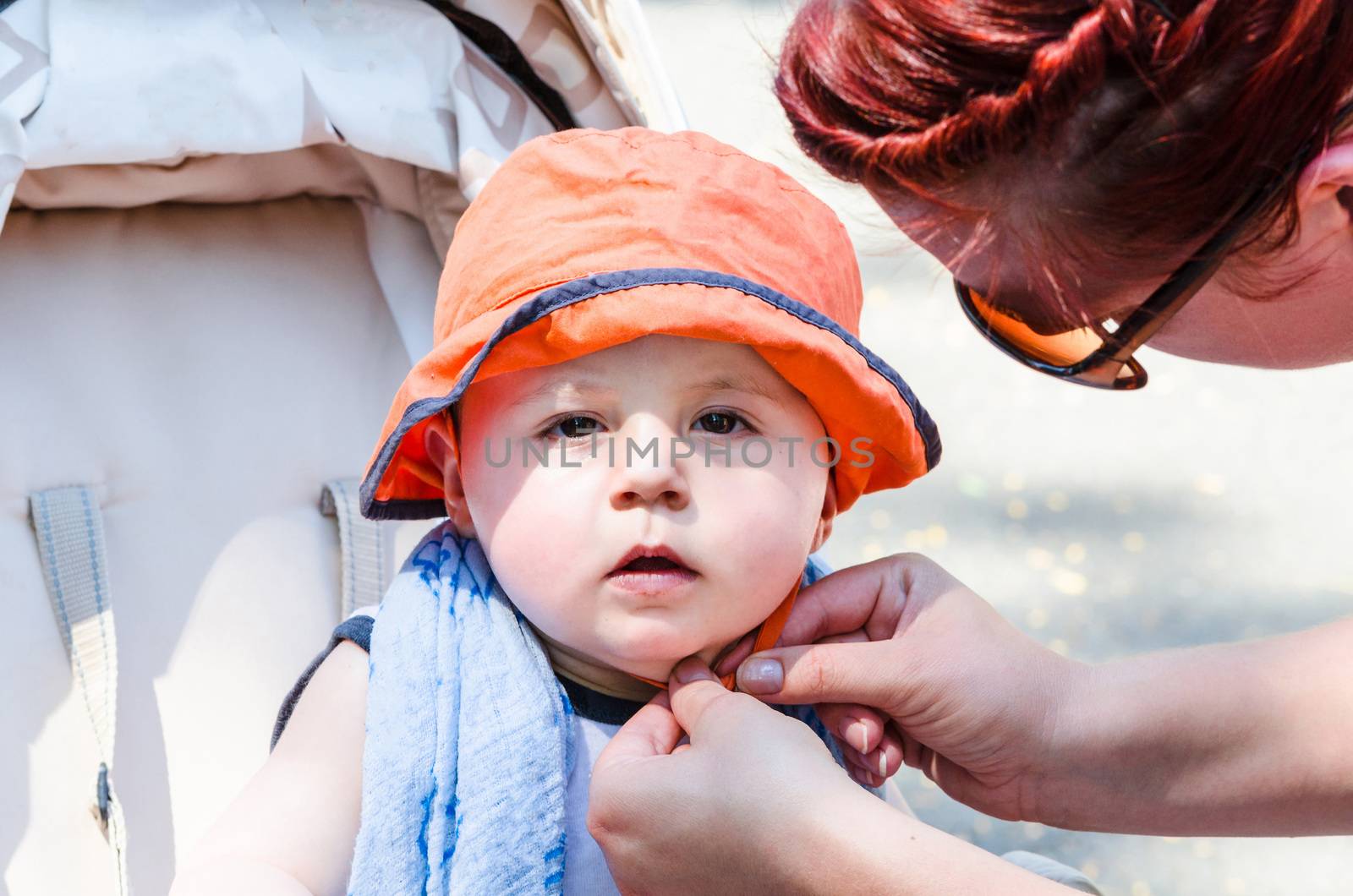 
Baby with orange cap sitting in a stroller, looking amazed. Background isolated.