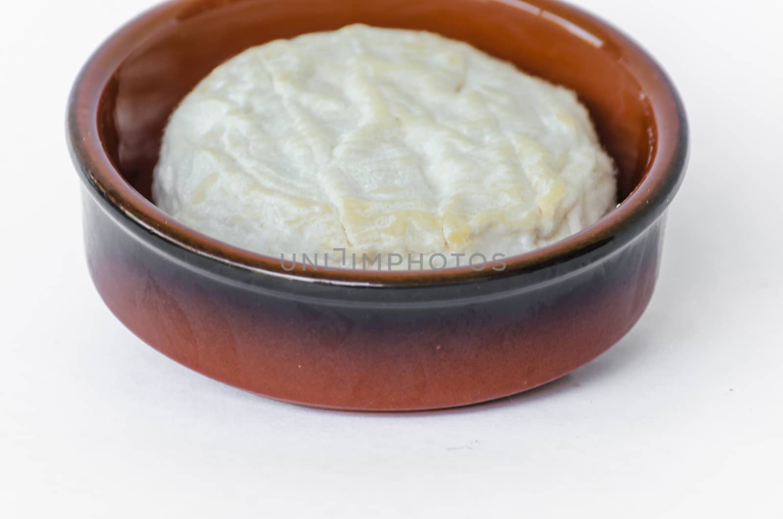 Round white Camembert in brown porcelain bowl.