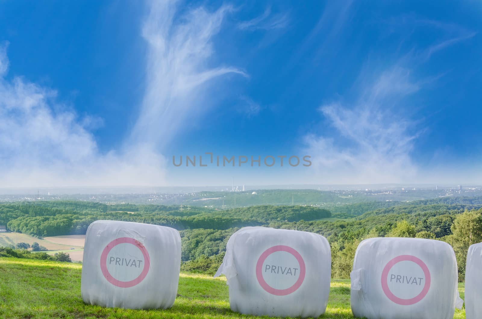 Three straw bales in white plastic film on a field with the Icon Private