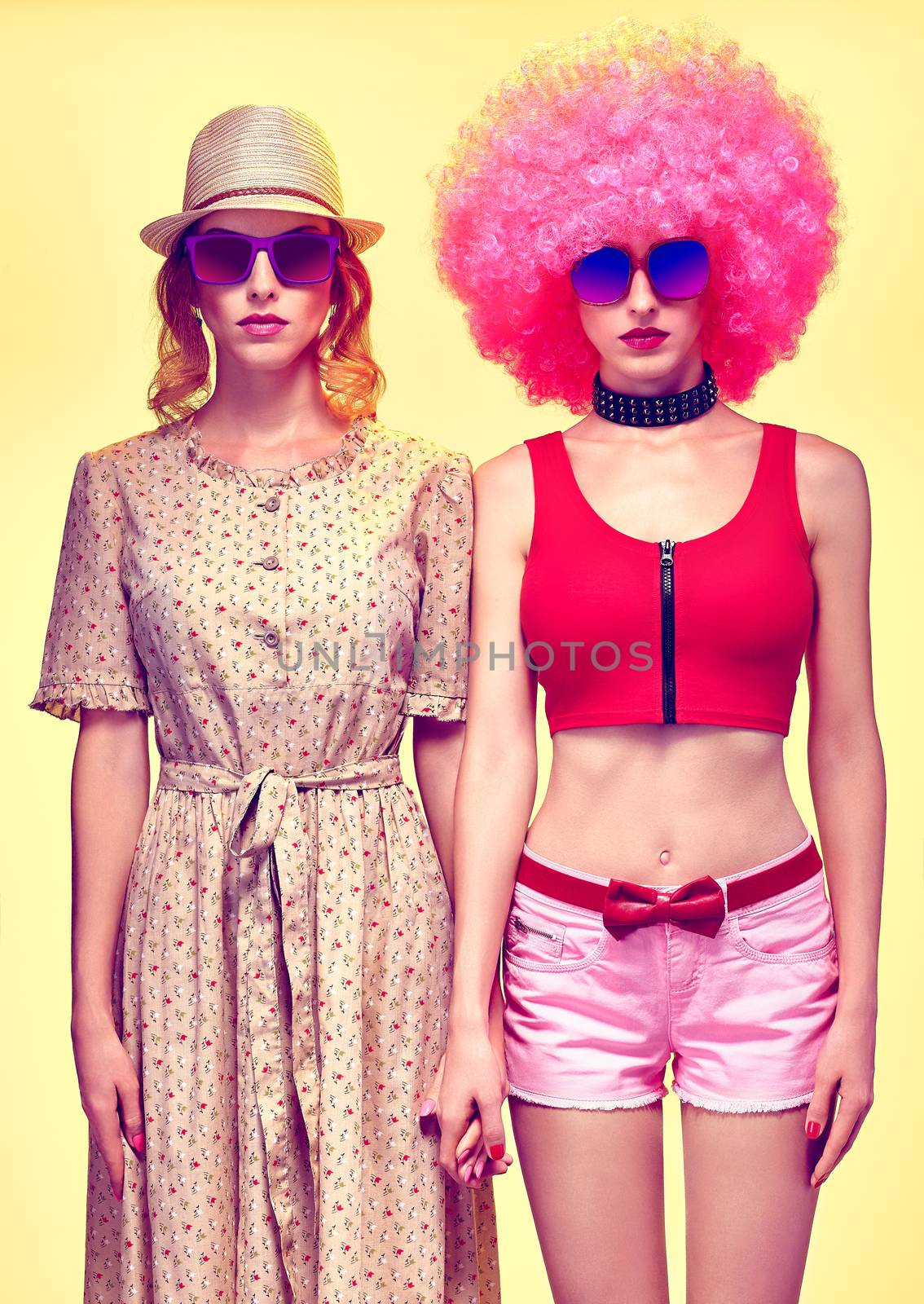 Fashion beauty people. Sexy hipster woman in stylish clothes, sisters, friends. Unusual party look. Vivid punk girl in sunglasses, hat, pink afro hairstyle on yellow. Provocative attractive playful 