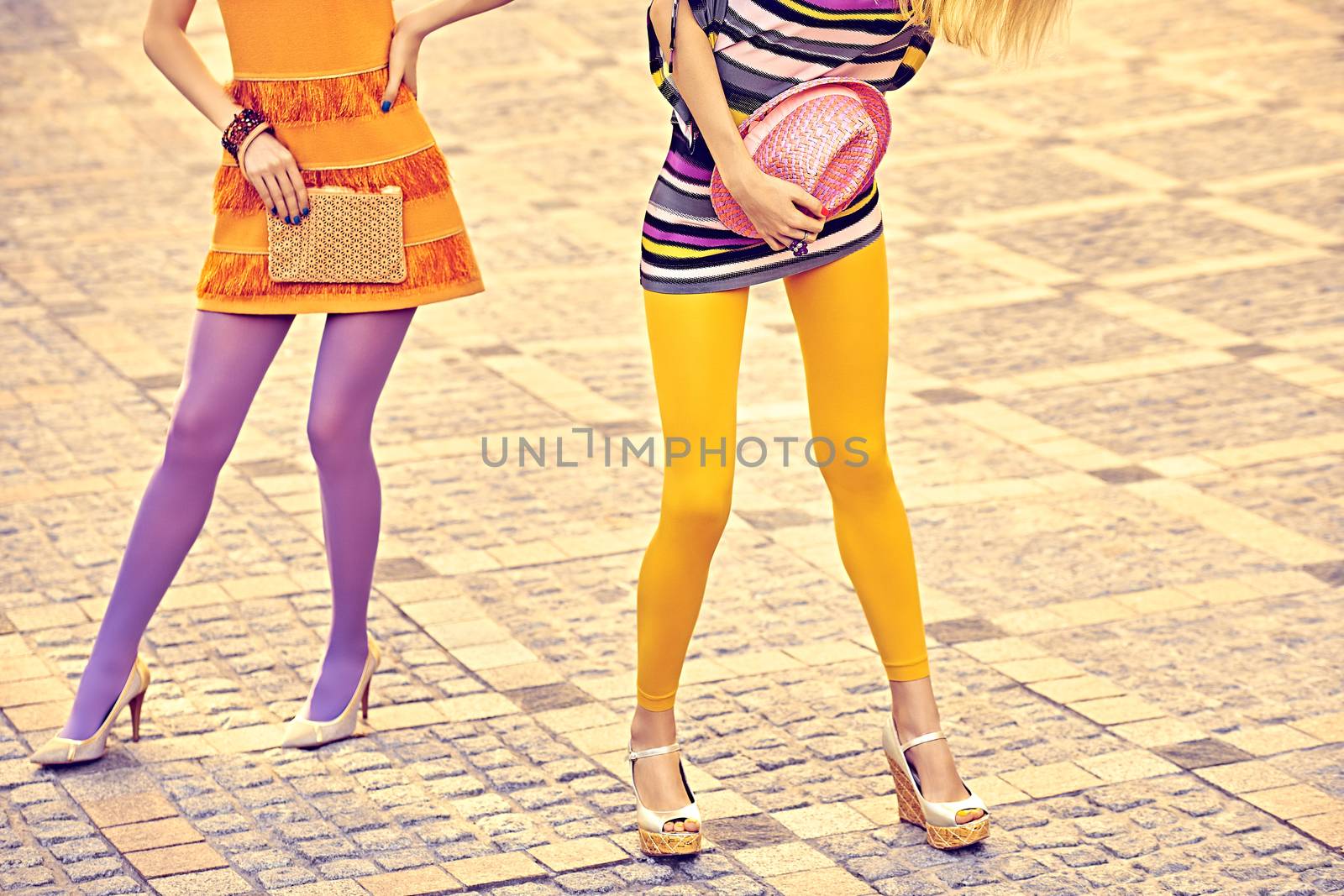 Fashion urban beauty people, friends, outdoor. Womens sexy legs, pantyhose, stylish shoes, clutches. Playful hipster girls in trendy dresses on paving stone, creative unusual pose. Vivid disco party 