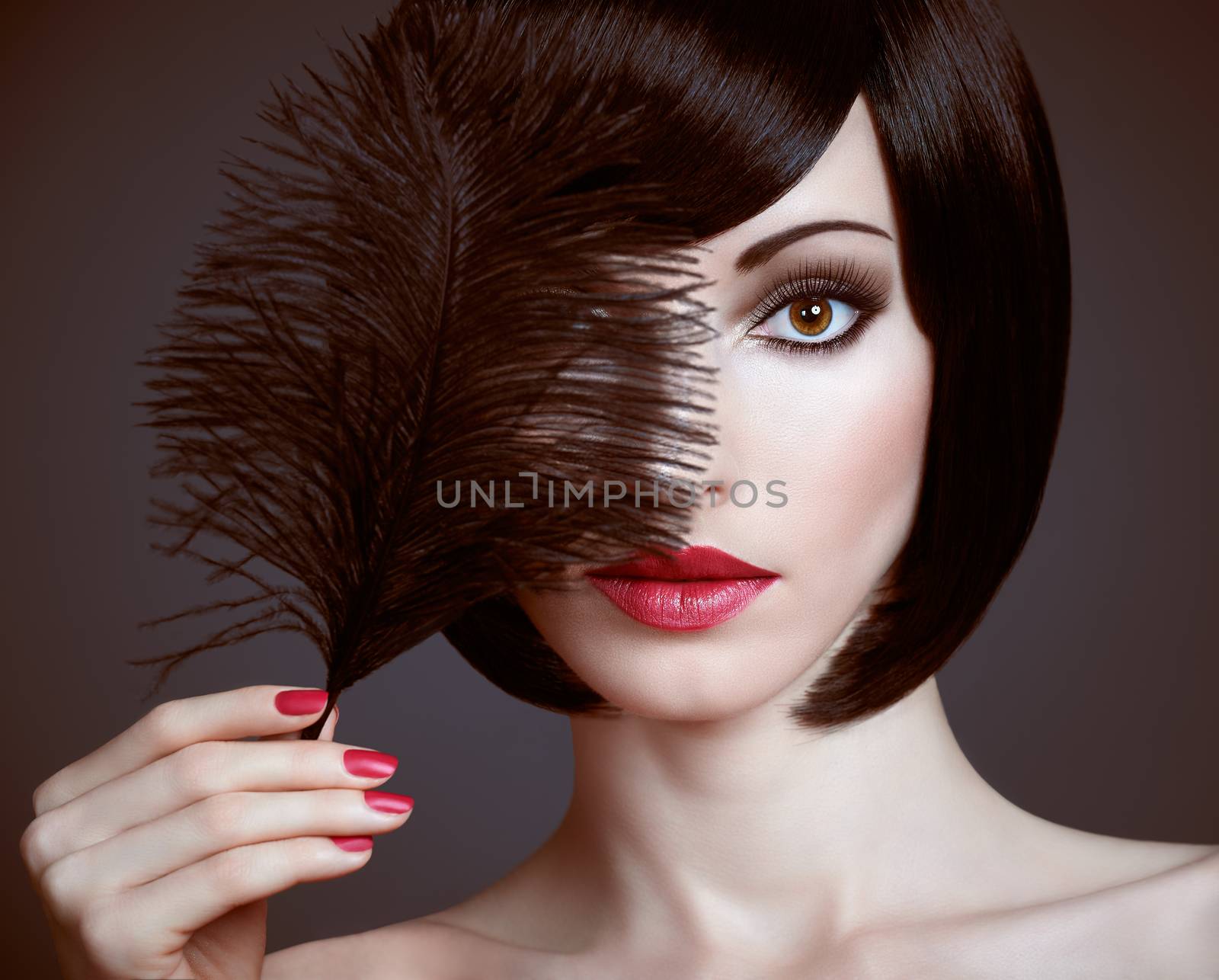Fashion beauty portrait of nude brunette woman with silky bob hairstyle on dark. Sensual lady mysteriously looks, covering eye by black feather. Brown-eyed girl, makeup, red lips. People face closeup