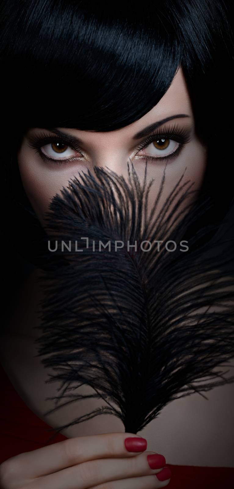 Fashion beauty portrait of sexy brunette woman with silky bob hairstyle on dark. Sensual lady mysteriously looks, covering face by black feather. Brown-eyed girl, makeup, red lips. People face closeup