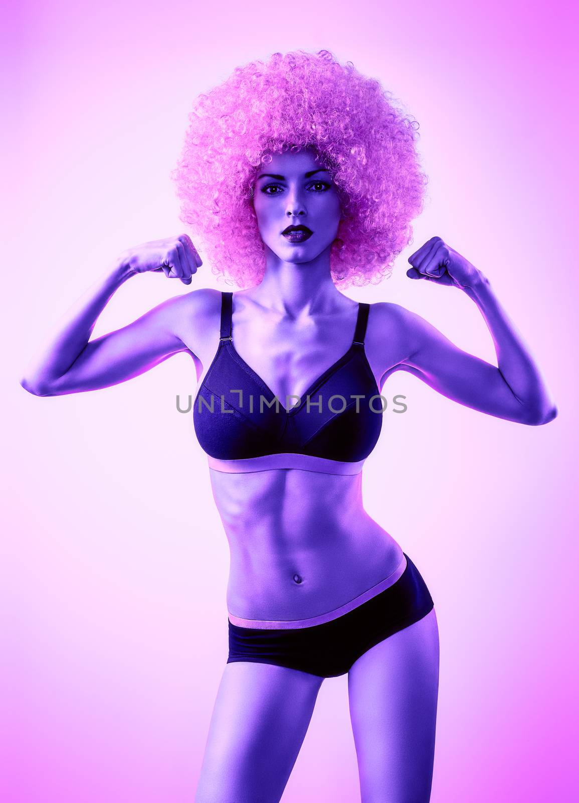 Beauty fashion. Fitness woman, unusual look. Sexy athletic body, people. Provocative attractive girl posing in trendy sport bra, shorts with afro hairstyle, purple background, copyspace, toned