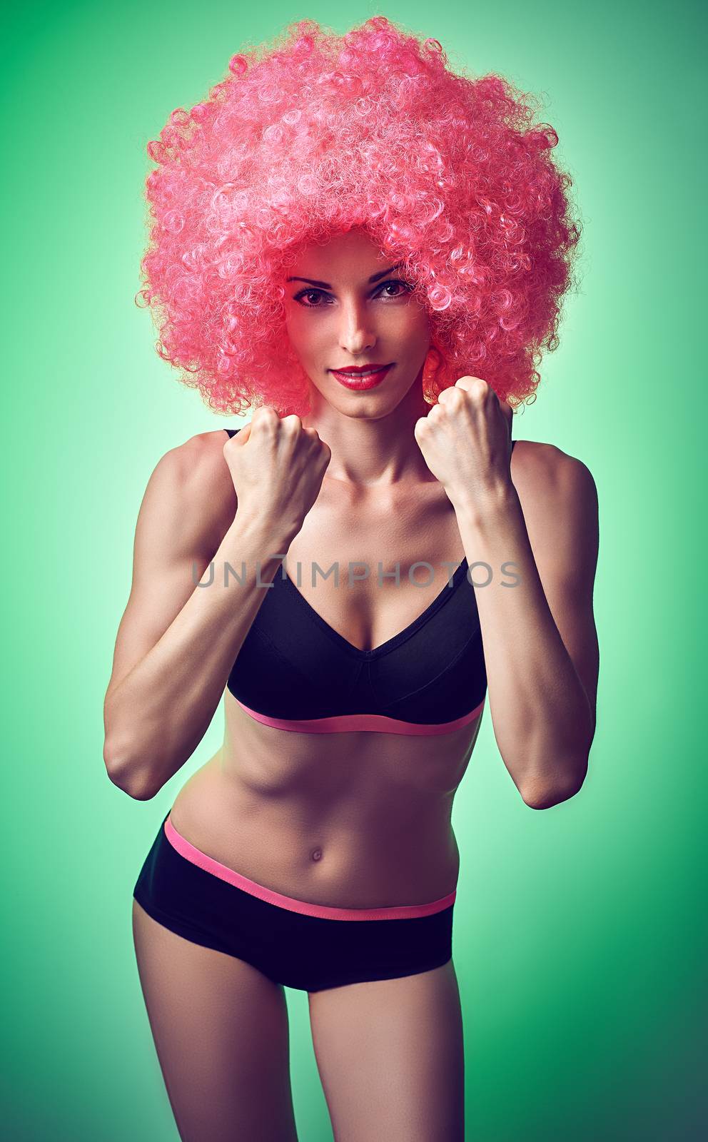 Beauty fashion. Fitness woman smiling, unusual look. Sexy athletic body, people. Provocative attractive girl posing in trendy sport bra, shorts with afro hairstyle, green background, copyspace, toned