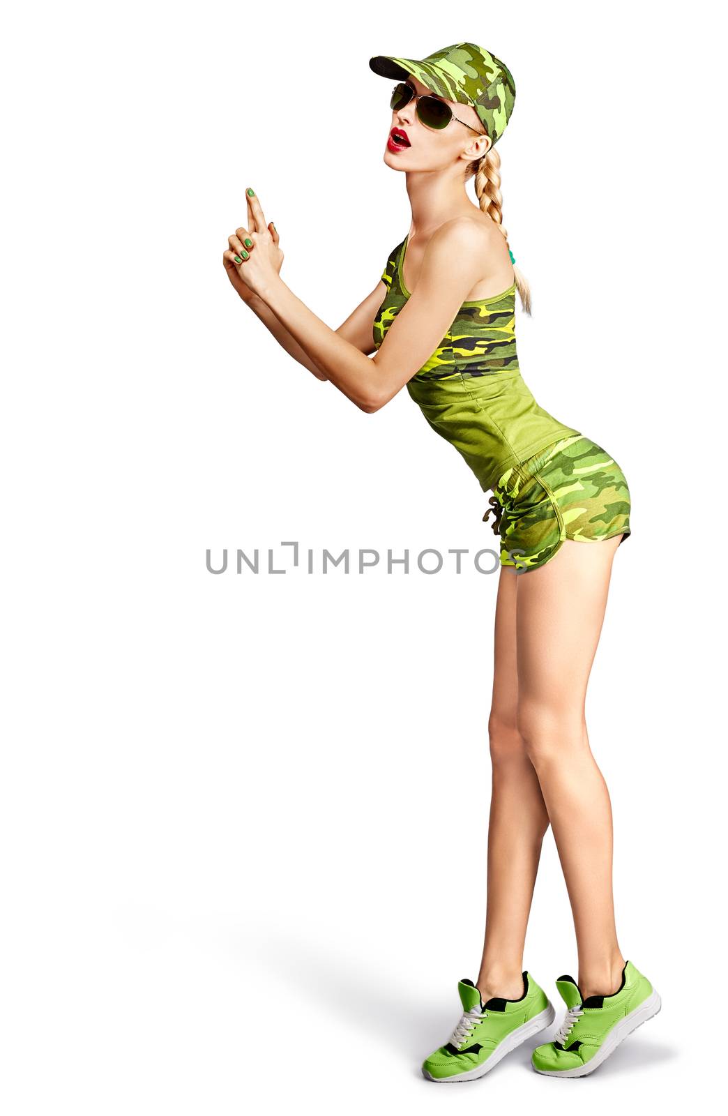 Fashion woman in camouflage clothes. Army beauty sexy military girl doing hands like a gun. Stylish playful people, unusual khaki green look, isolated on white. Attractive blond girl makes gun gesture