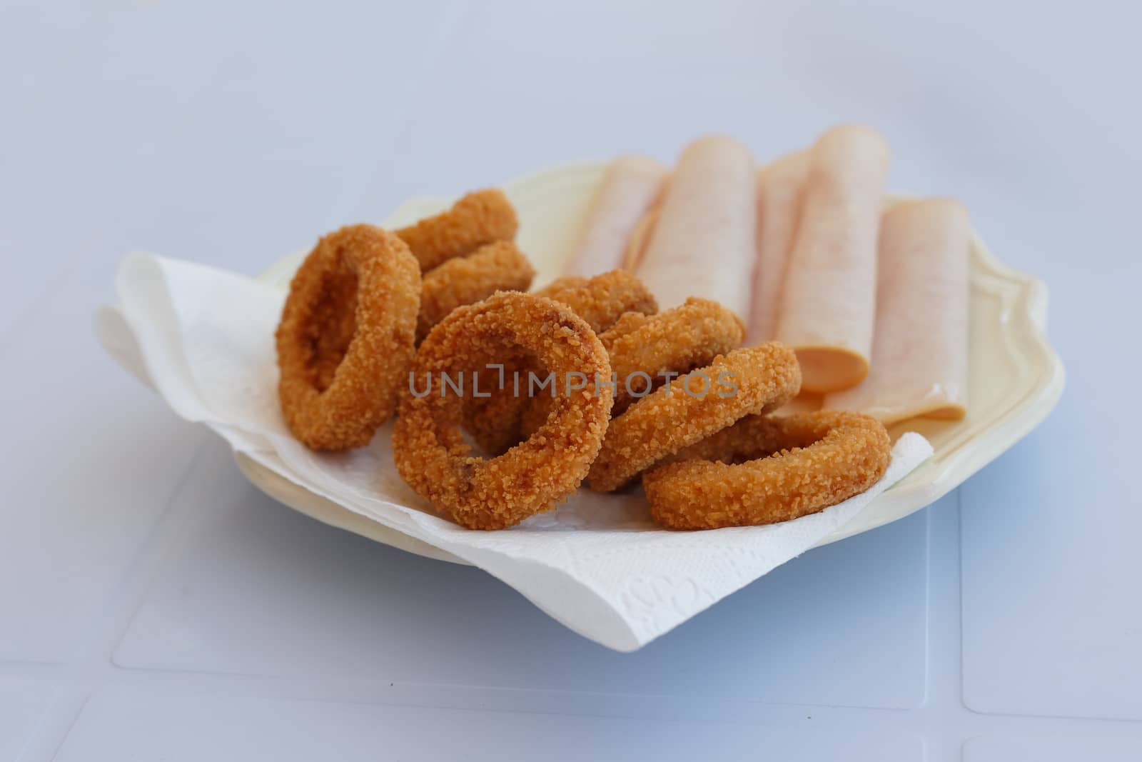 Close up detailed front view of a plate of fried onion rings with jambon served on a plate.