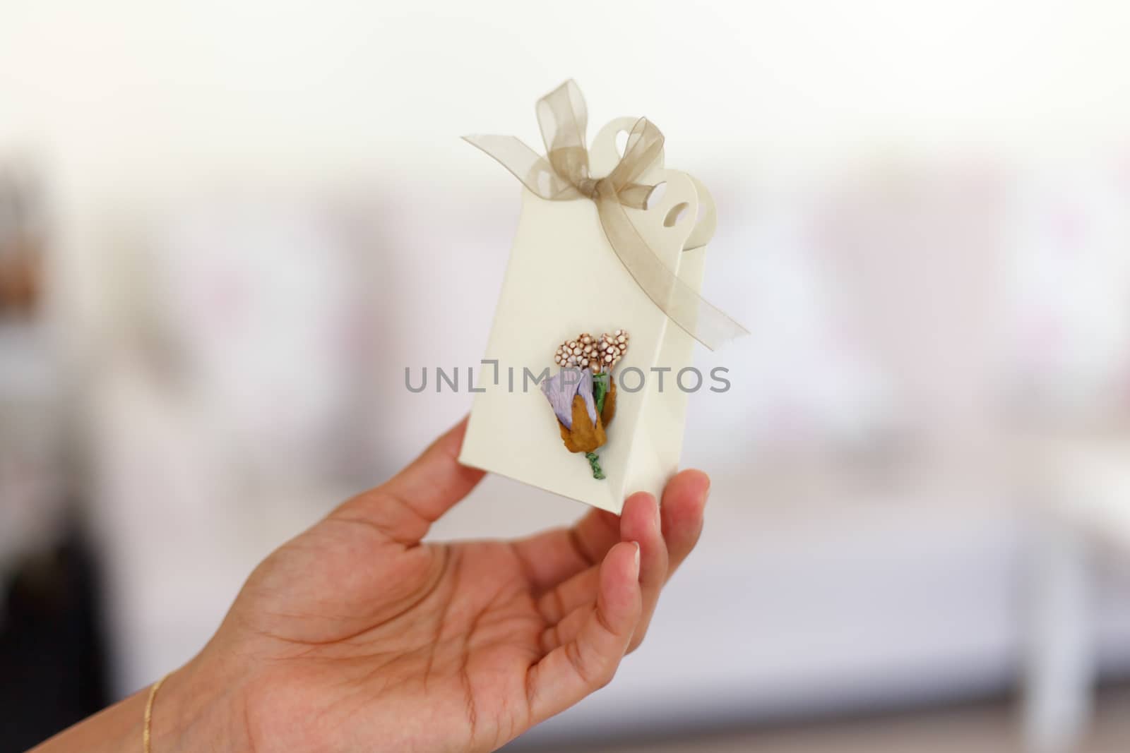 Close up detailed front view of hand-crafted white gift box holding on hand with small flowers and colorful ribbons.