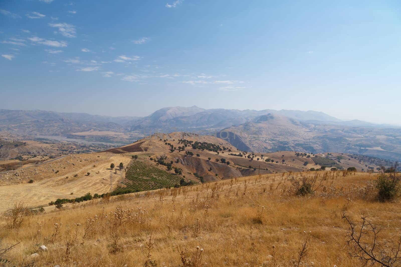 View of barren hills and high mountains with small trees, on cloudy blue sky background.
