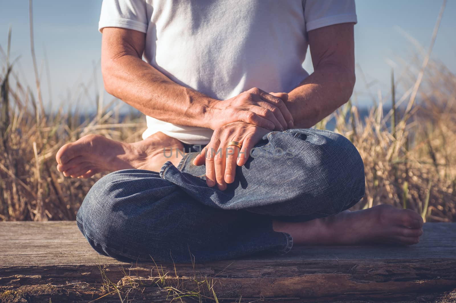 Man sitting in a relaxed yoga pose at the beach.