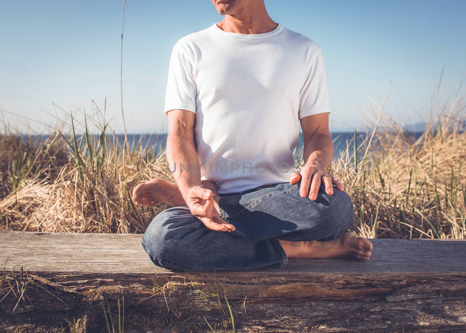 Man sitting in a relaxed yoga pose at the beach.