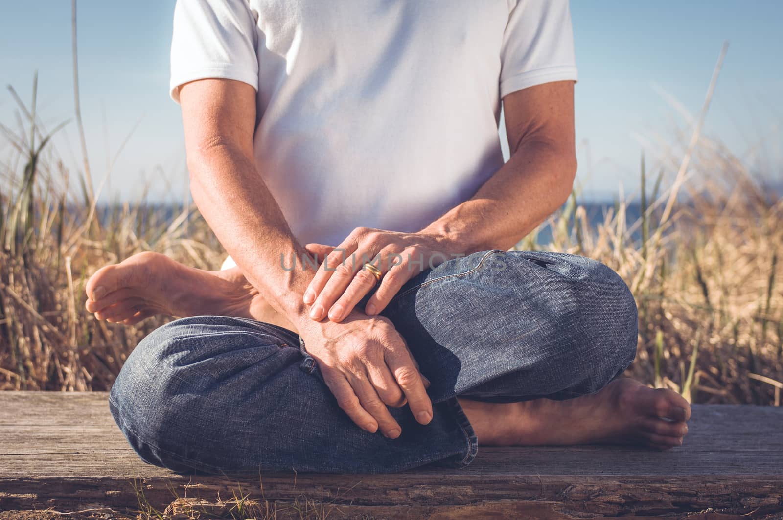 Man sitting in a relaxed yoga pose at the beach.