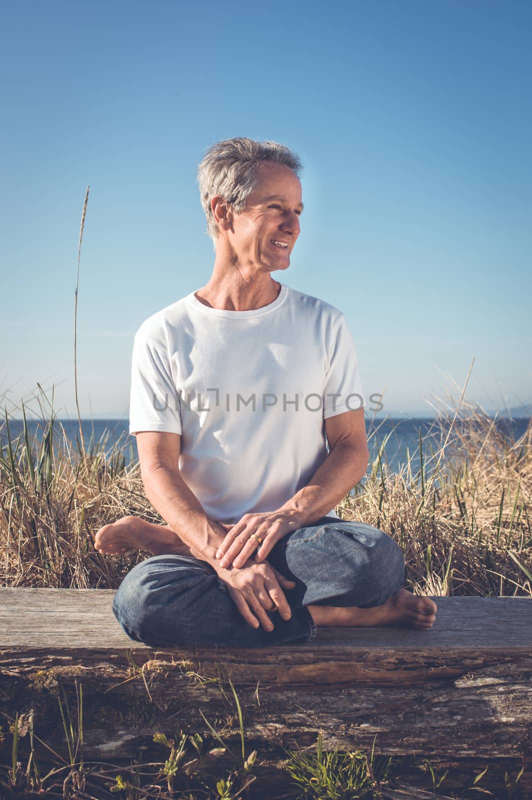 Man sitting in a relaxed yoga pose at the beach.