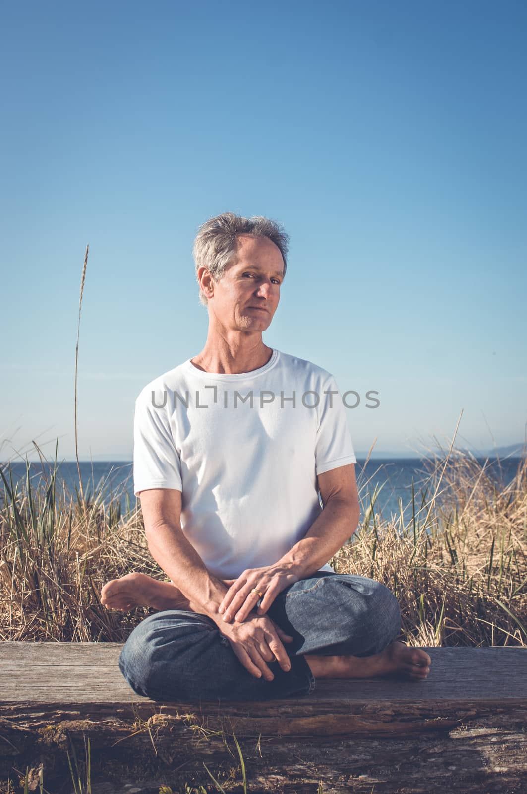 Man sitting in a relaxed yoga pose at the beach.