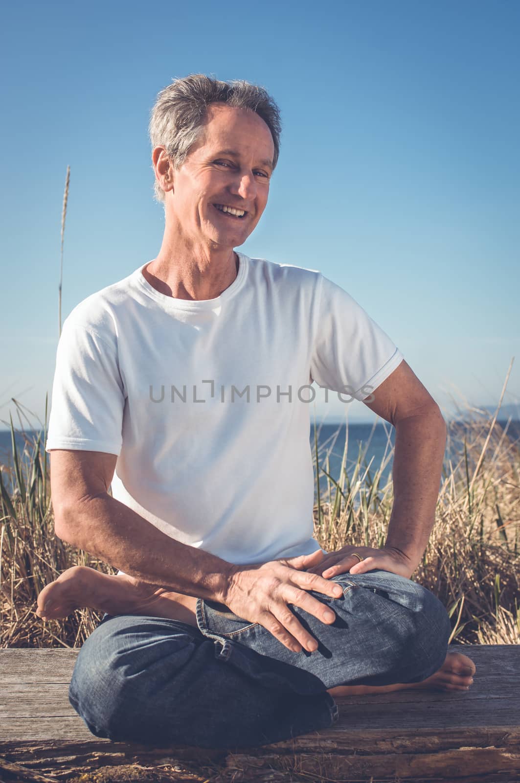 Man sitting in a relaxed yoga pose at the beach.