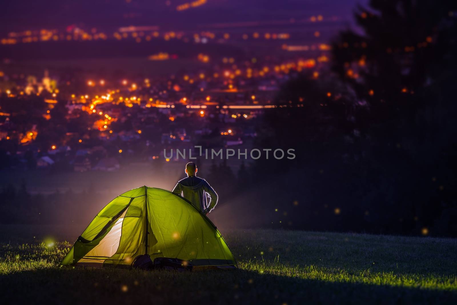 Countryside Camping with Scenic City View Down the Valley. Illuminated Cityscape at Night and the Camper with Illuminated Tent. Countryside Getaway.