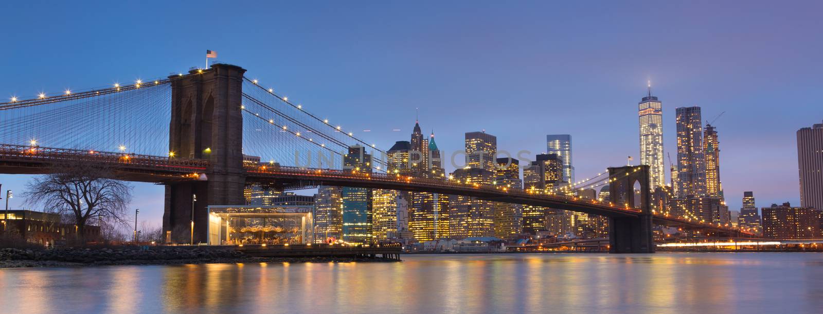 Brooklyn bridge and New York City Manhattan downtown skyline at dusk with skyscrapers illuminated over East River panorama. 