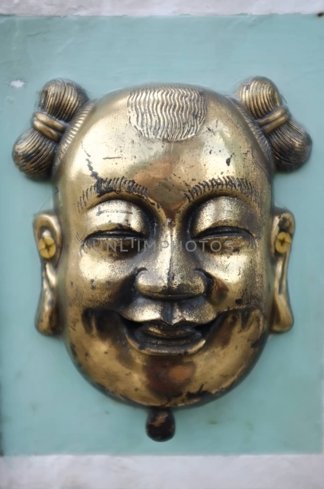 Brass or bronze chinese mask on green cement wall by Hepjam