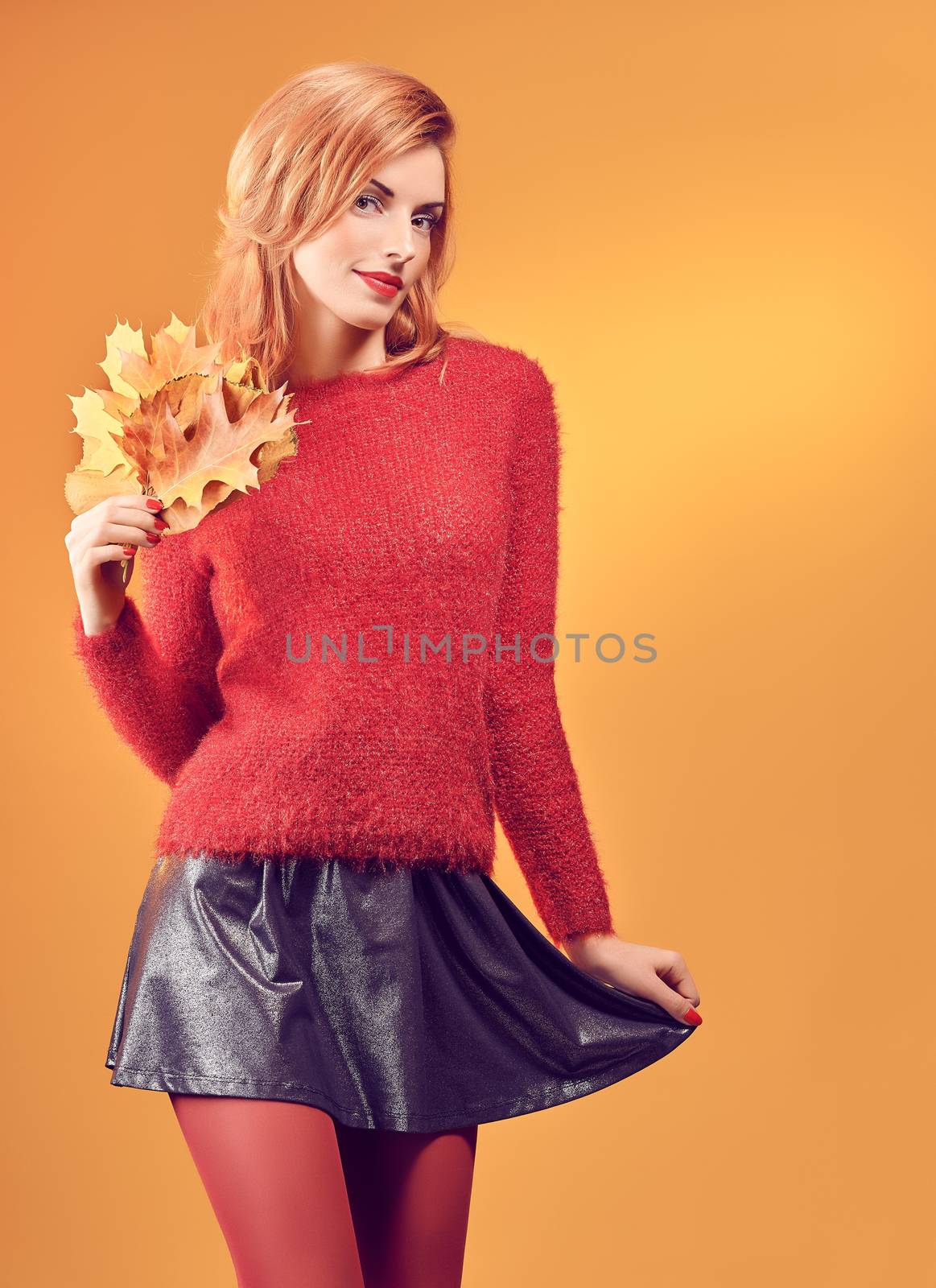 Beauty portrait redhead young model woman, autumn leafs in hands. Attractive happy playful girl in stylish red sweater smiling, people.Retro, vintage, creative toned.Orange yellow background,copyspace