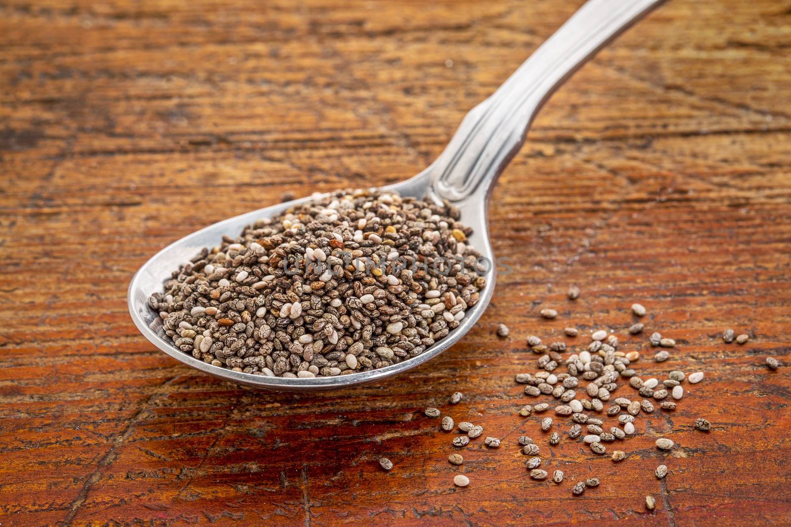tablespoon of chia seeds against rustic, scratched wood table