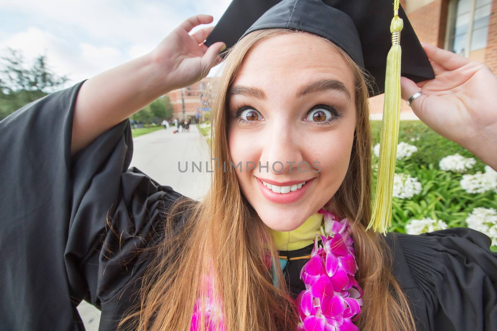Excited wide-eyed female graduate student holding her cap