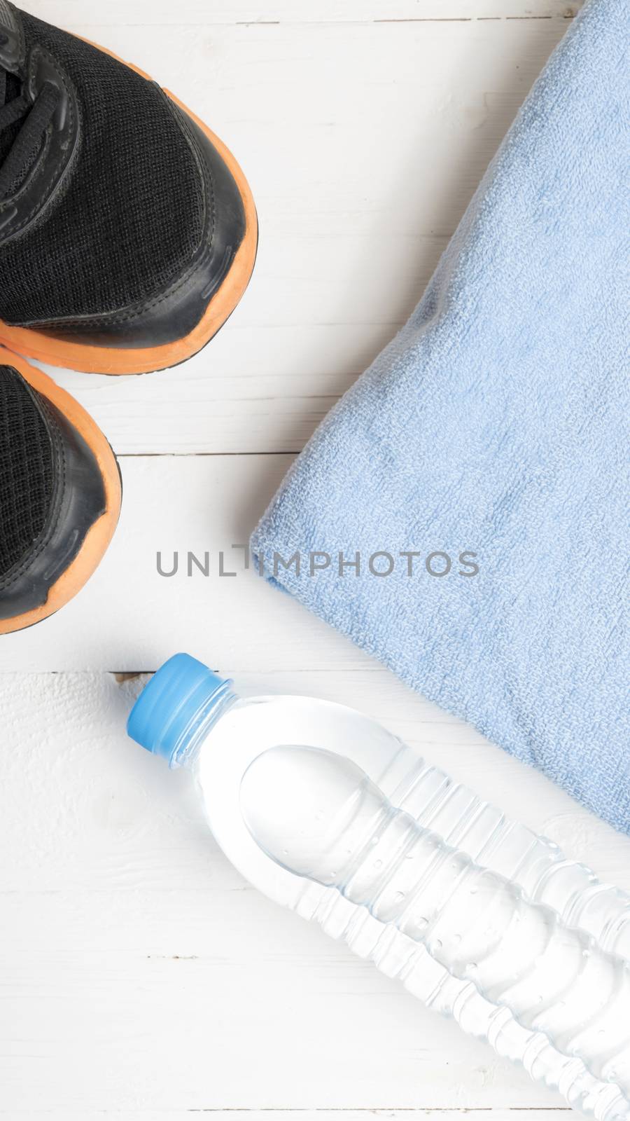 fitness equipment:blue towel,drinking water and running shoes on white wood table