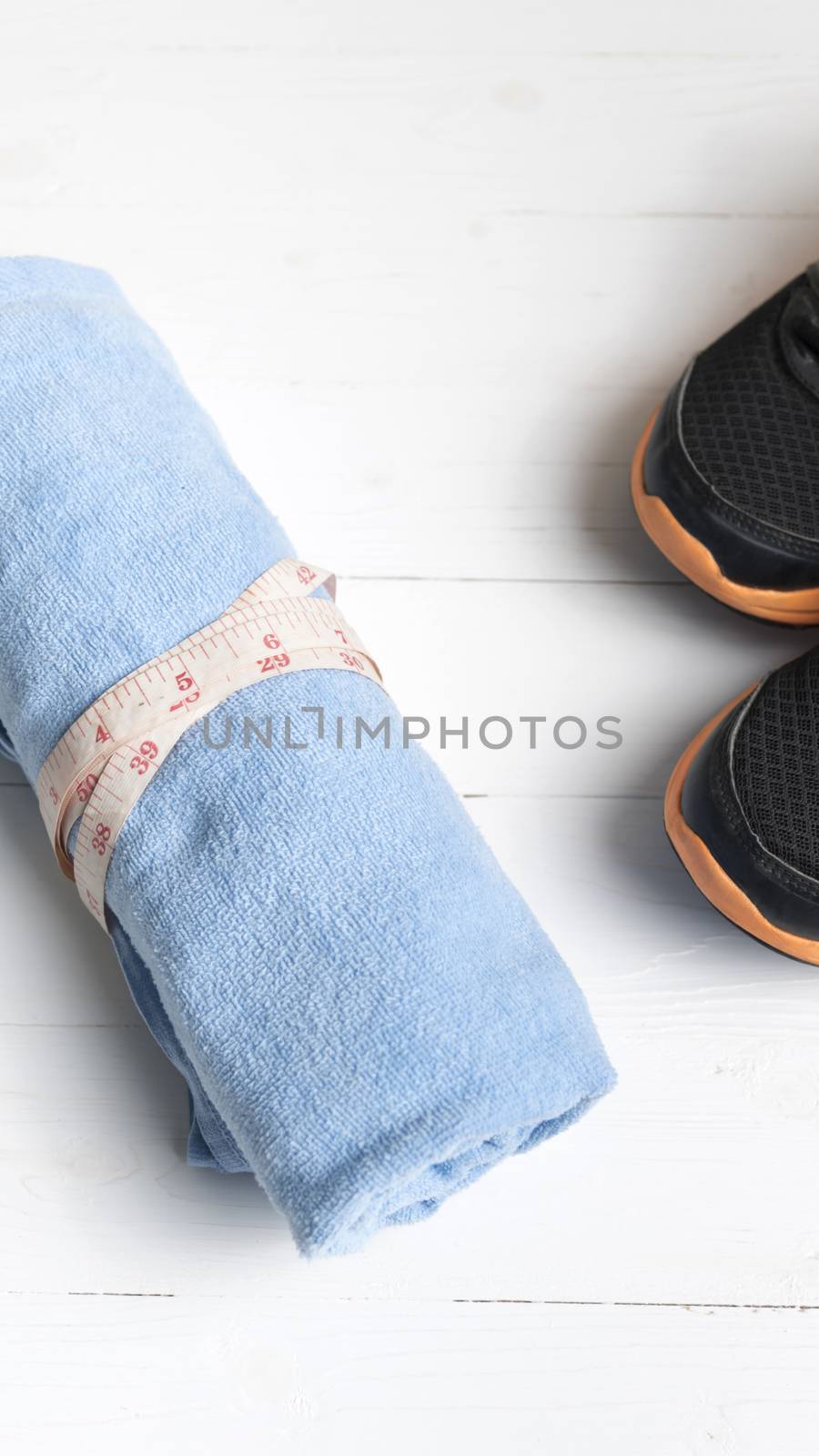 fitness equipment : running shoes,blue towel and measuring tape on white wood table