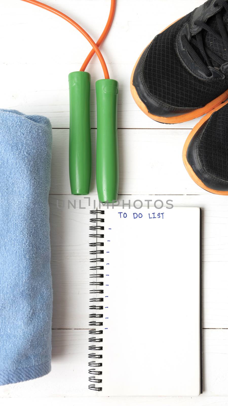 fitness equipment : running shoes,towel,jumping rope and notebook write to do list on white wood table