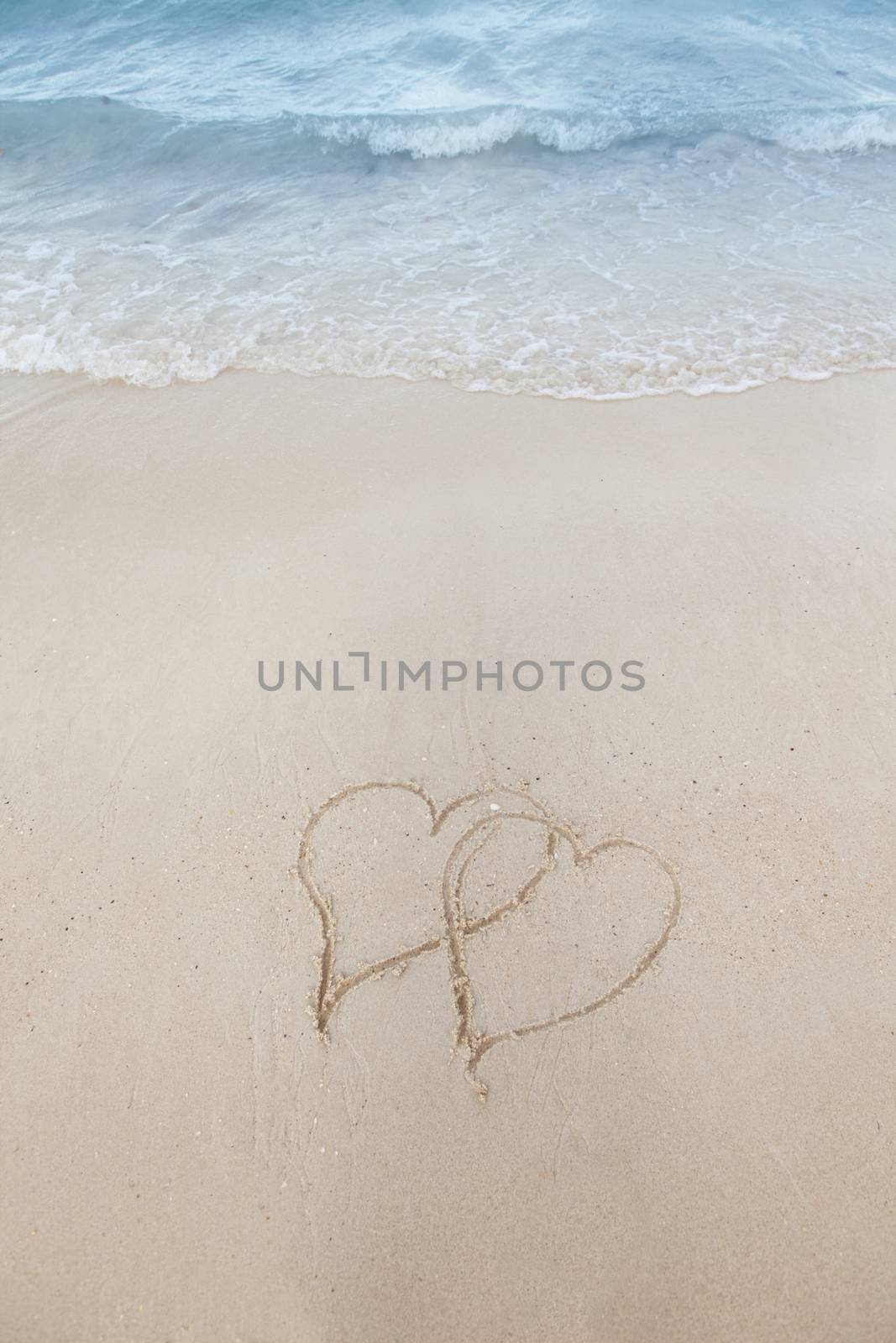 Love on beach concept - two hearts on a beach sand with coming wave