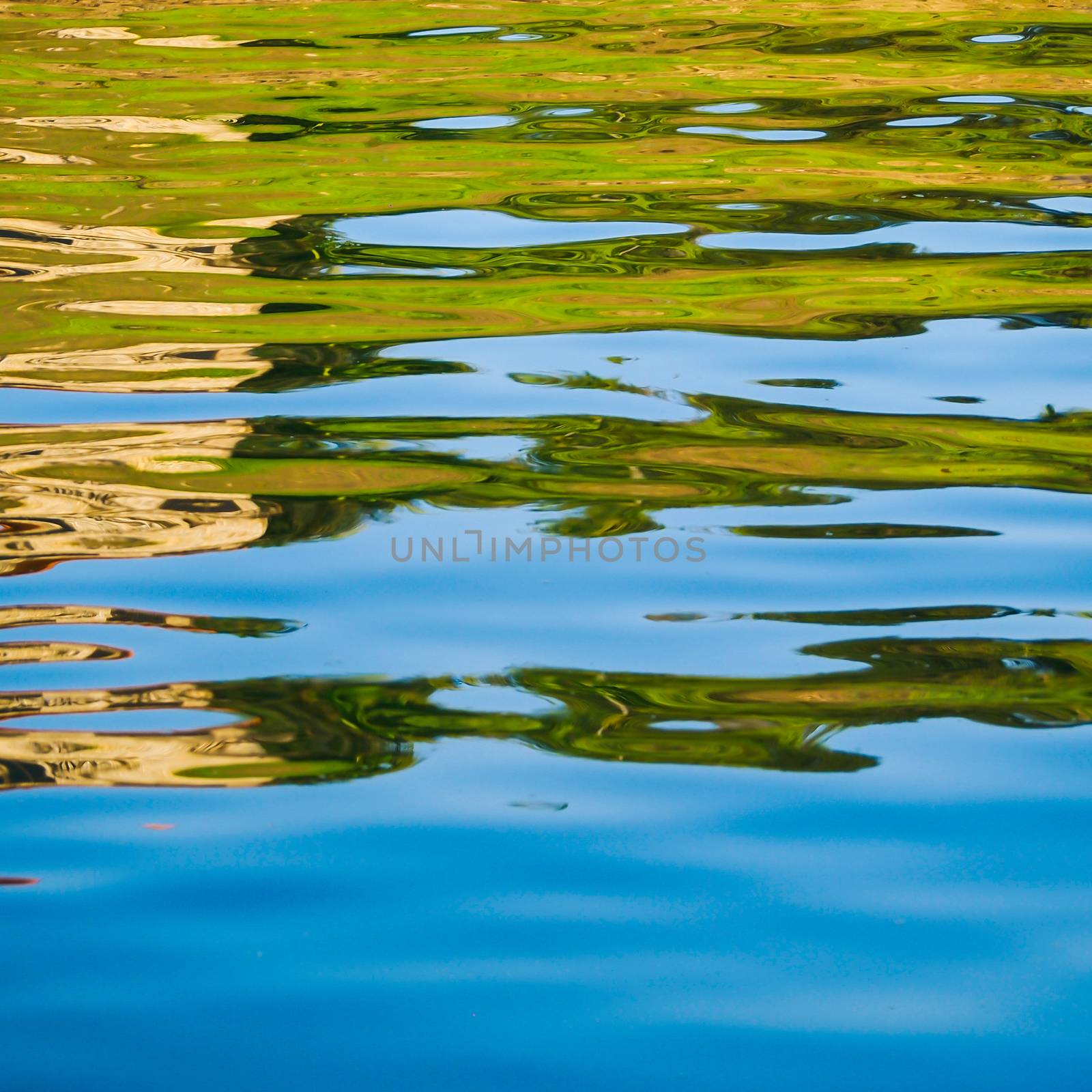 Colorful patterns of blue, brown and green are seen in reflections in the water of a lake
