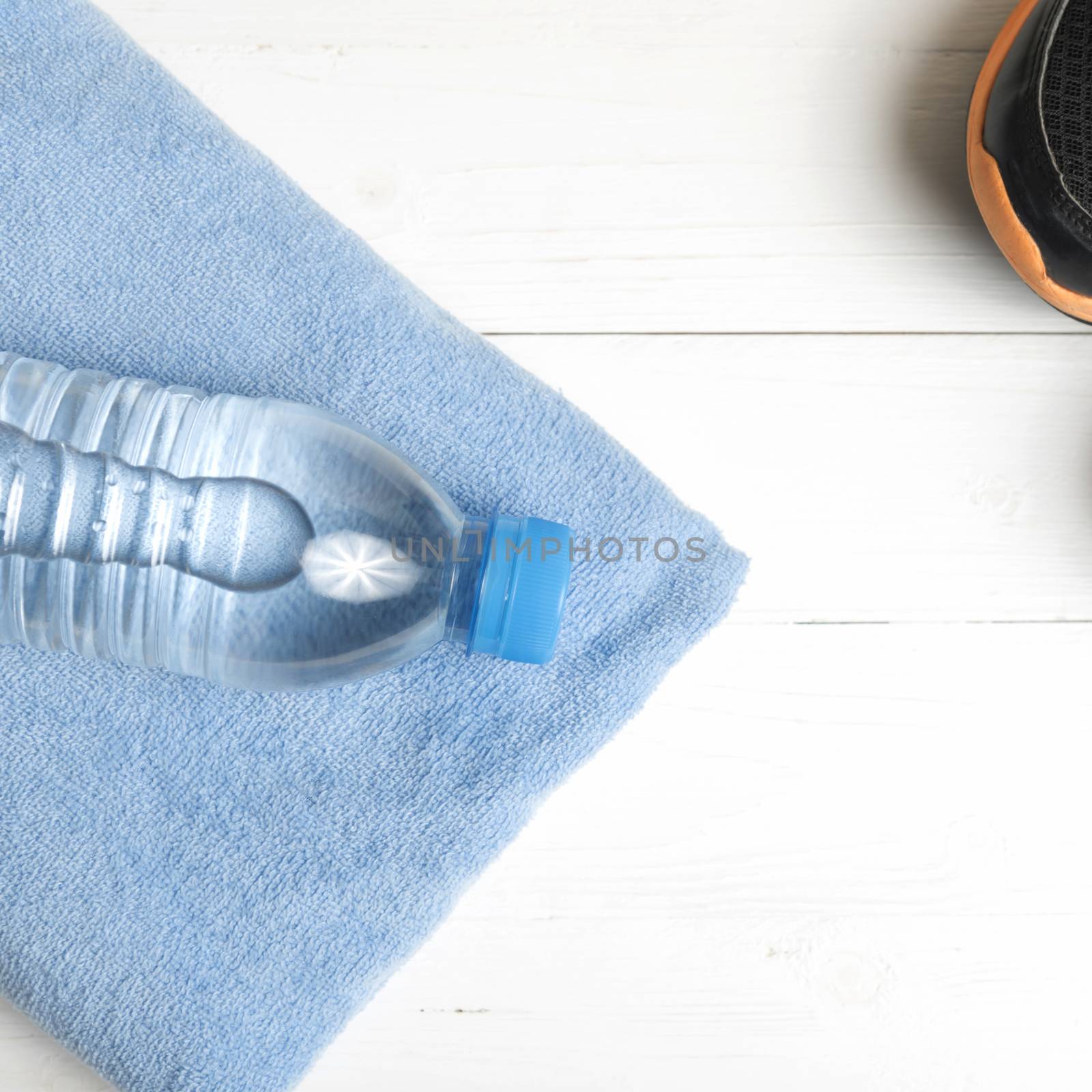 fitness equipment:blue towel,drinking water and running shoes on white wood table