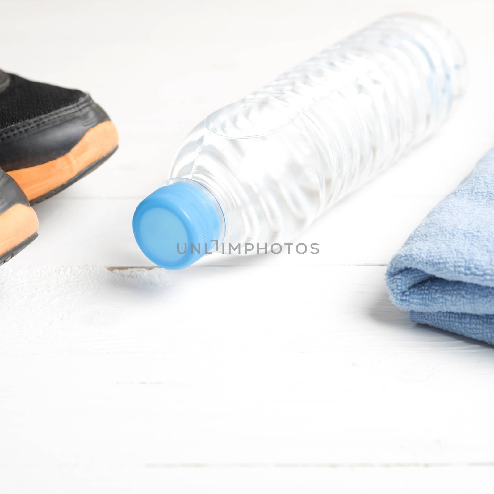 fitness equipment:blue towel,drinking water and running shoes on white wood table