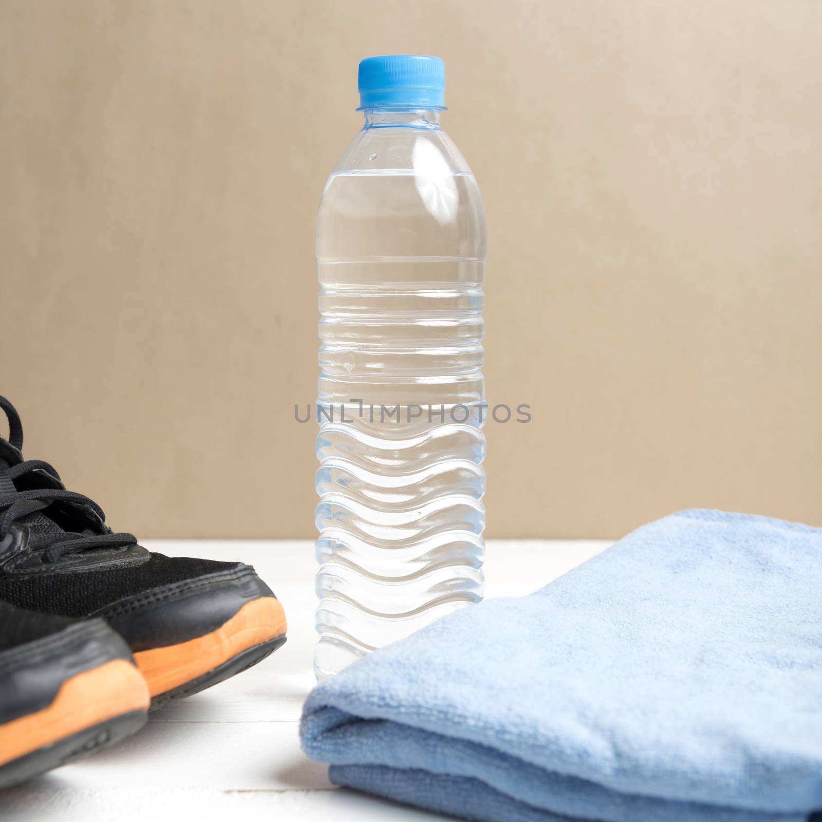 fitness equipment:blue towel,drinking water and running shoes on white wood table