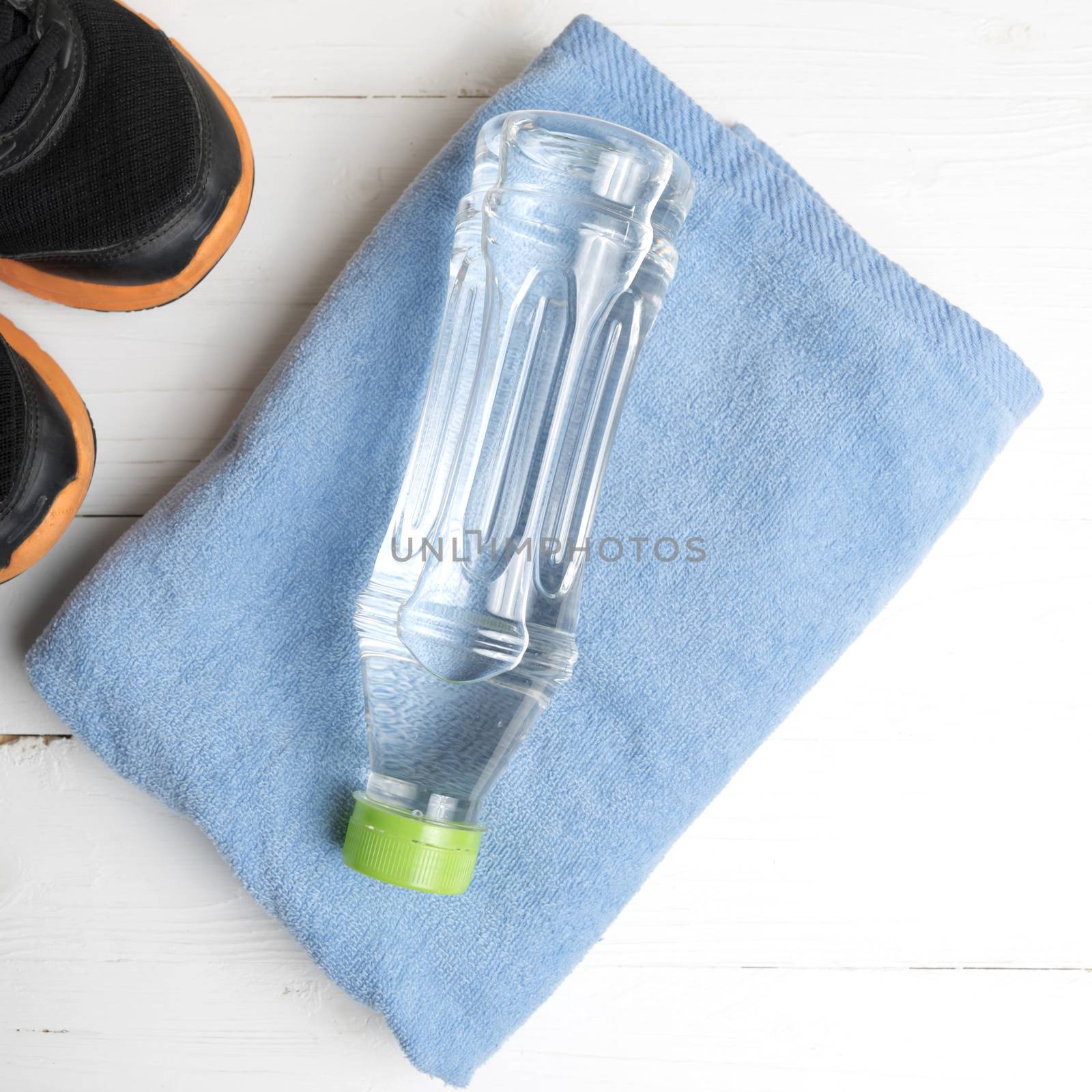 fitness equipment:blue towel,drinking water and running shoes on white wood table