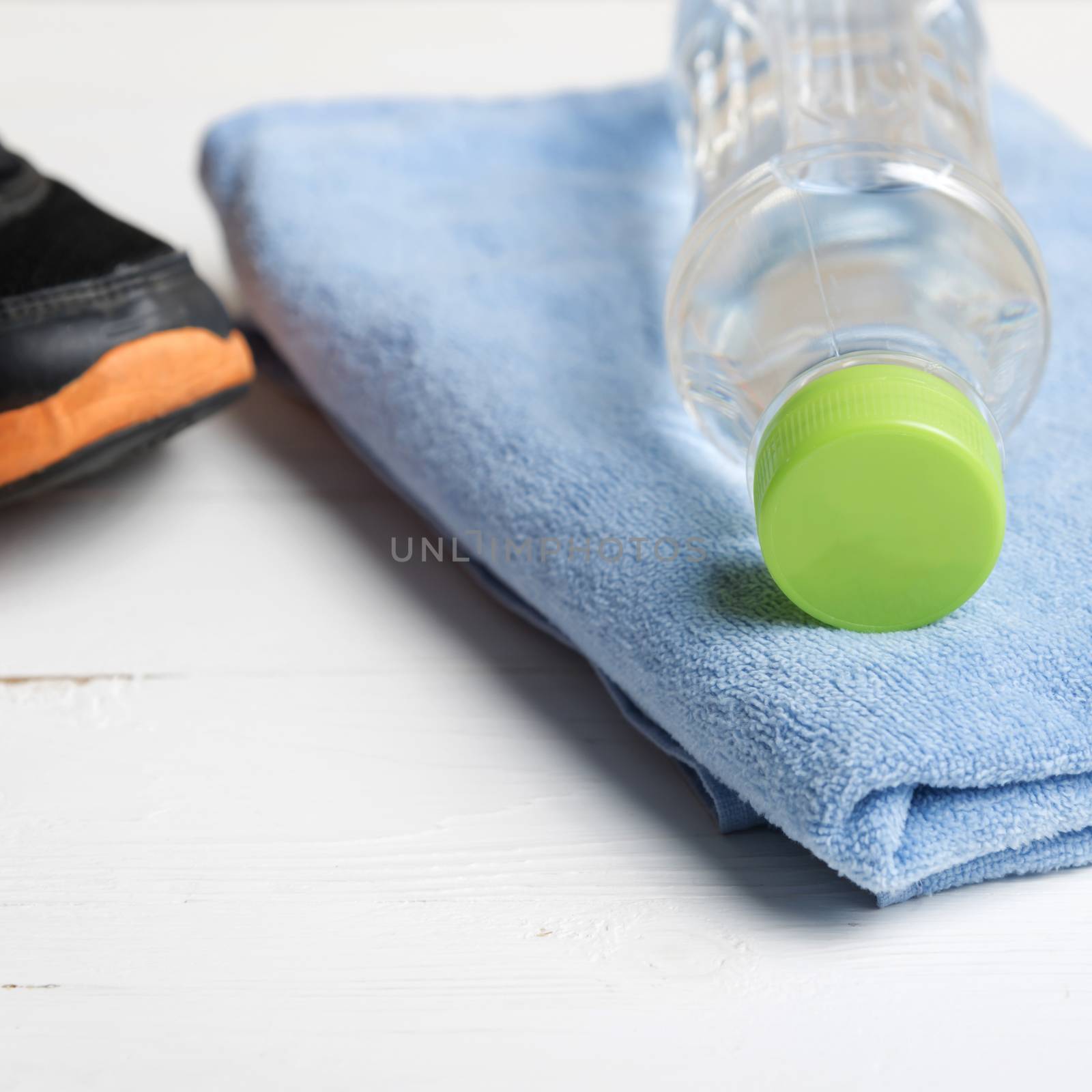 fitness equipment:blue towel,drinking water and running shoes on white wood table