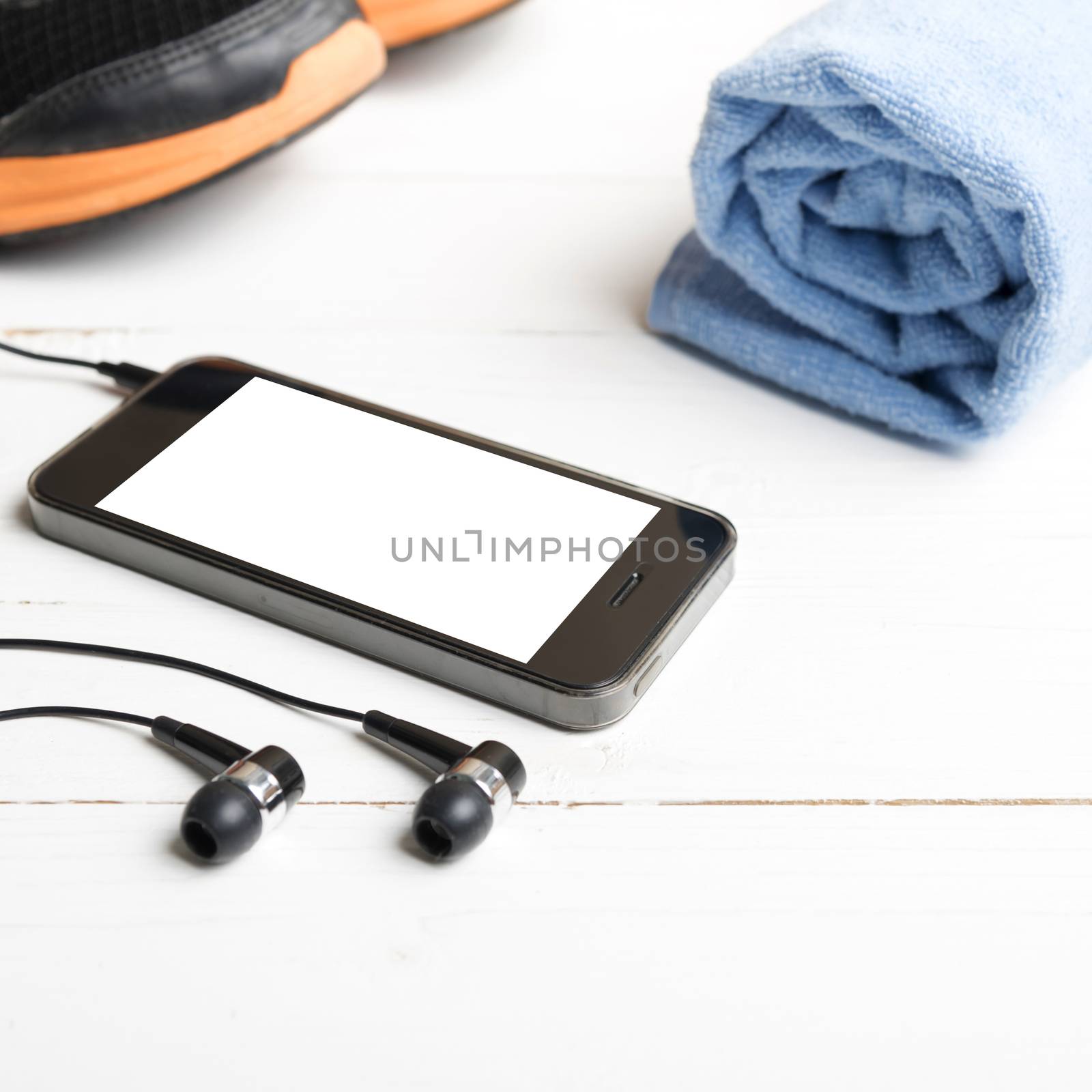 fitness equipment:running shoes,blue towel and smart phone on white wood table