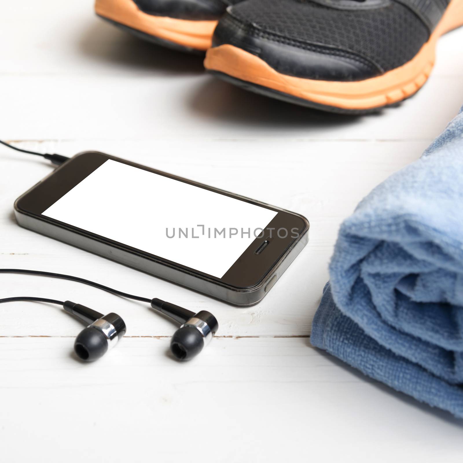 fitness equipment:running shoes,blue towel and smart phone on white wood table