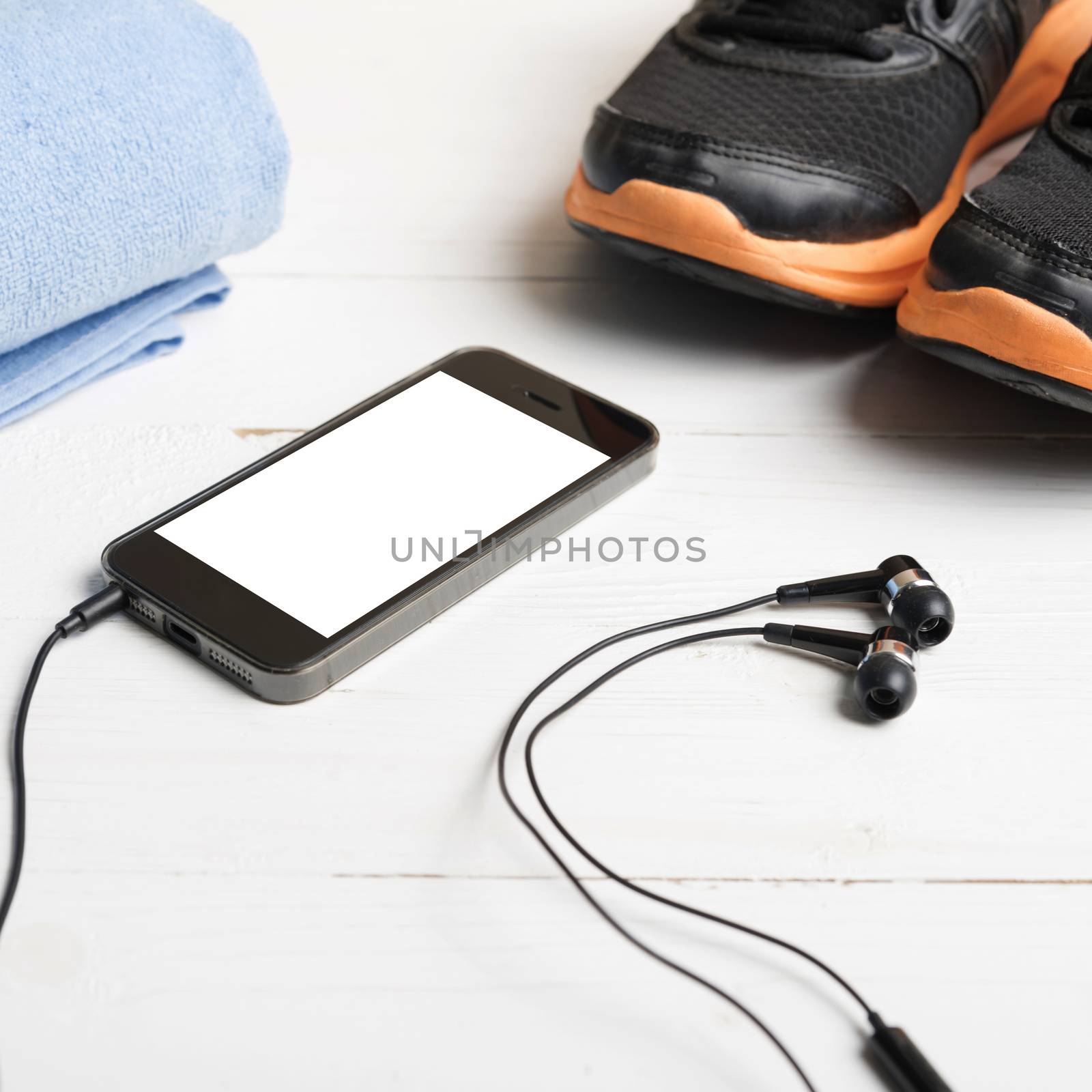 fitness equipment:running shoes,blue towel and smart phone on white wood table