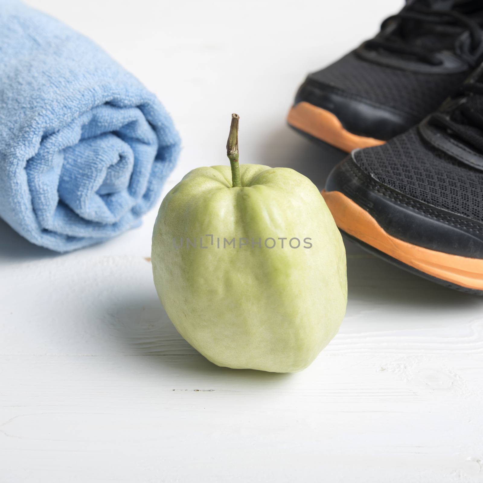 fitness equipment : running shoes,blue towel and guava fruit on white wood table