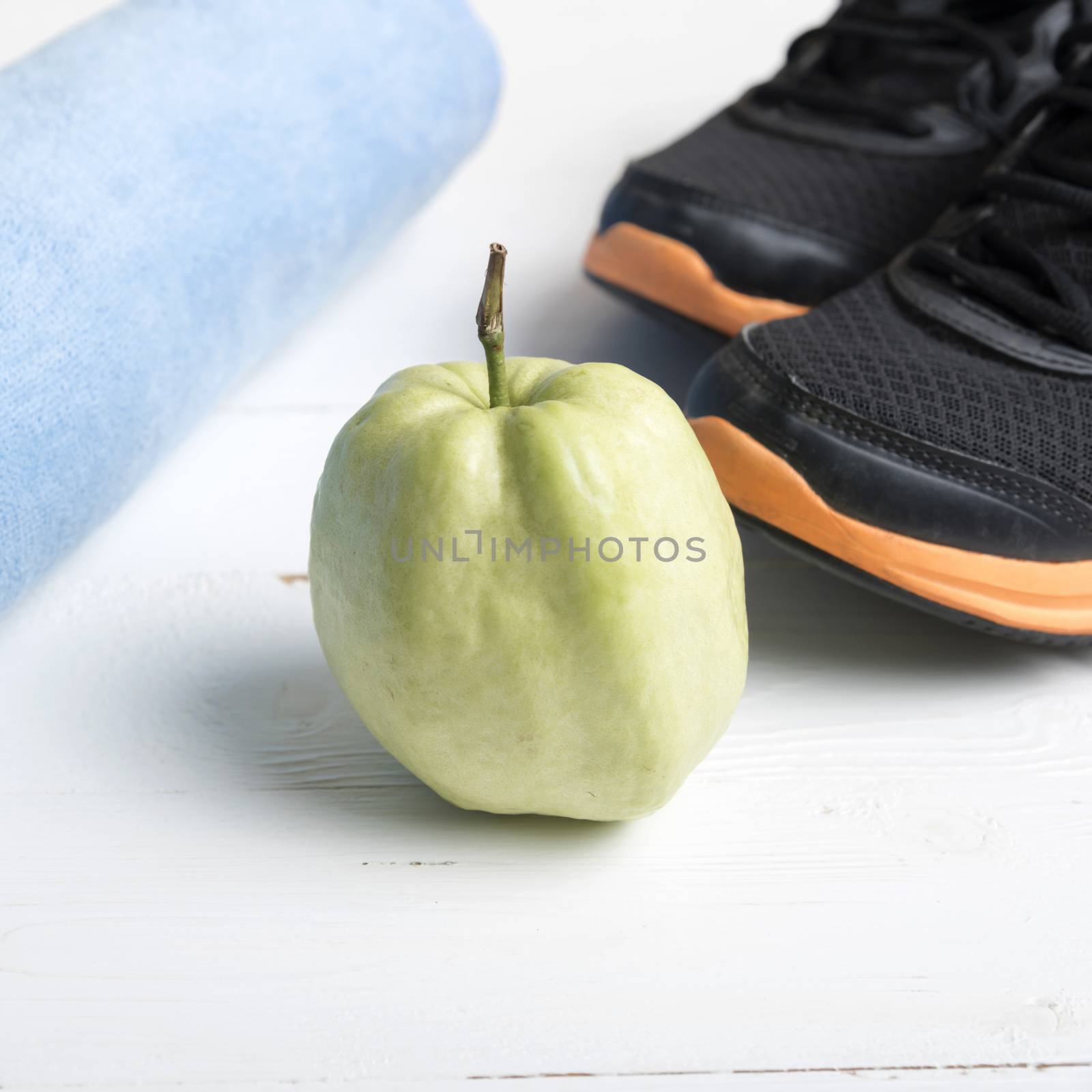 fitness equipment : running shoes,blue towel and guava fruit on white wood table