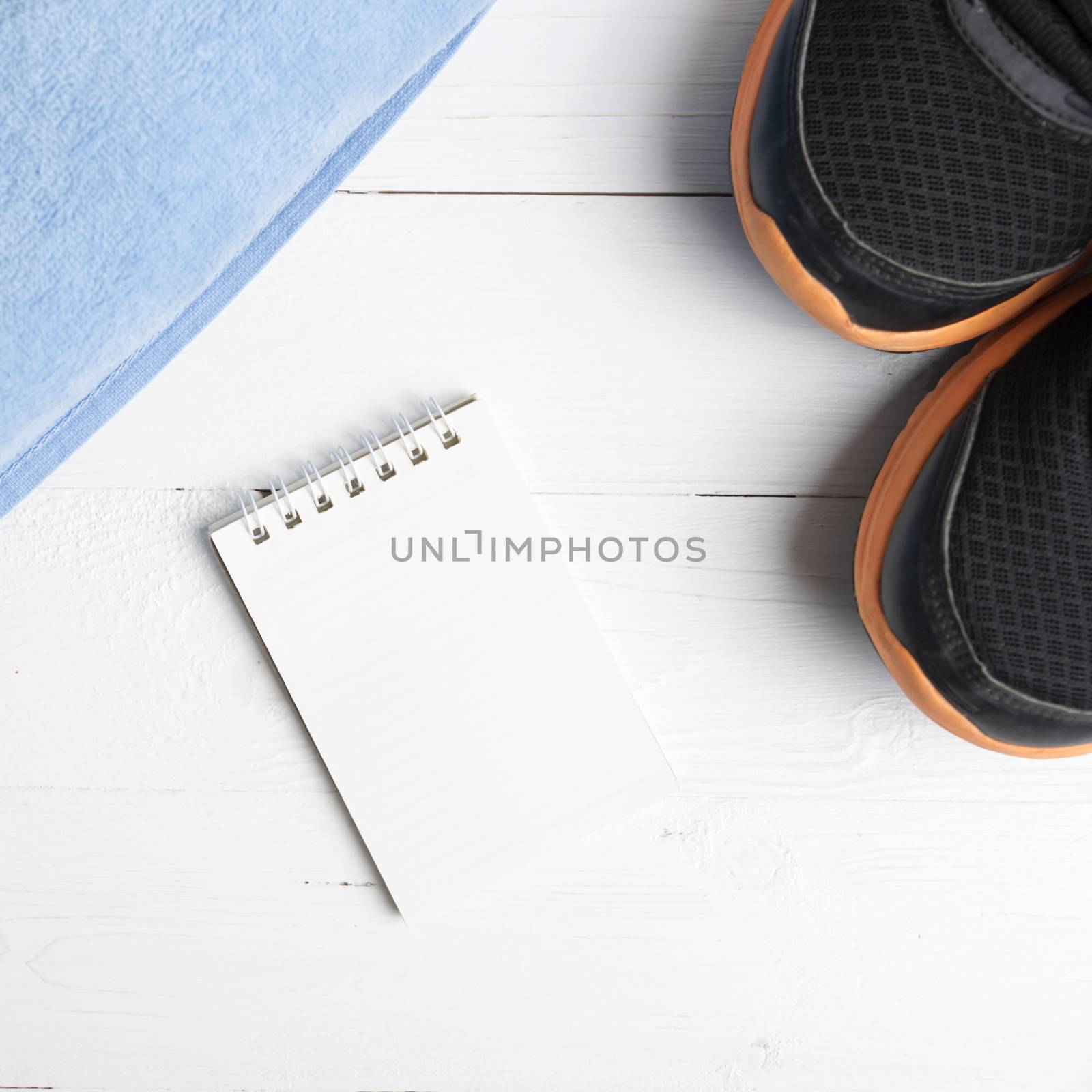 fitness equipment : running shoes,blue towel and notepad on white wood table