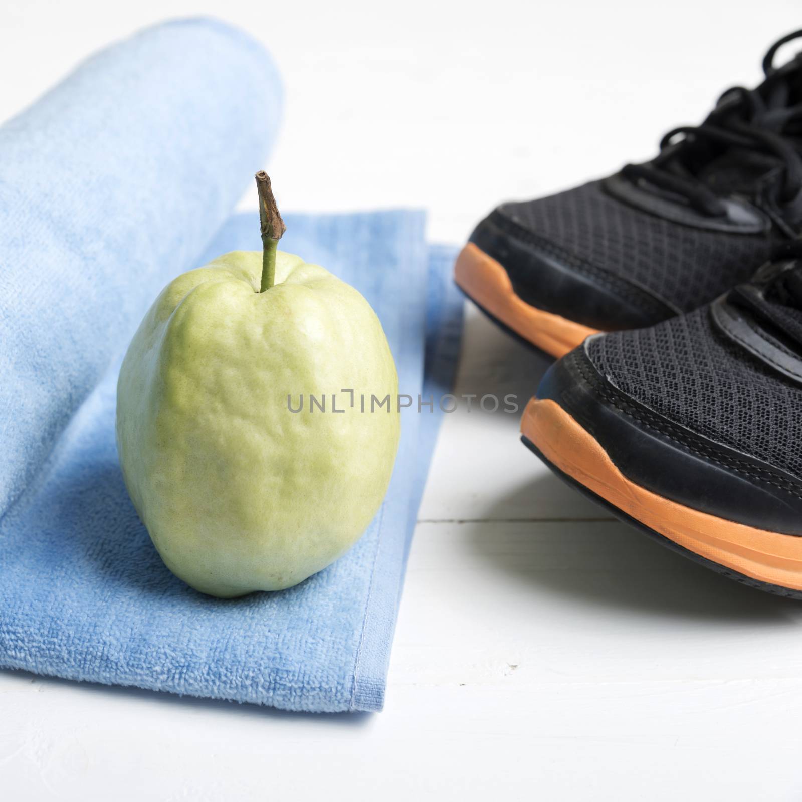 fitness equipment : running shoes,blue towel and guava fruit on white wood table