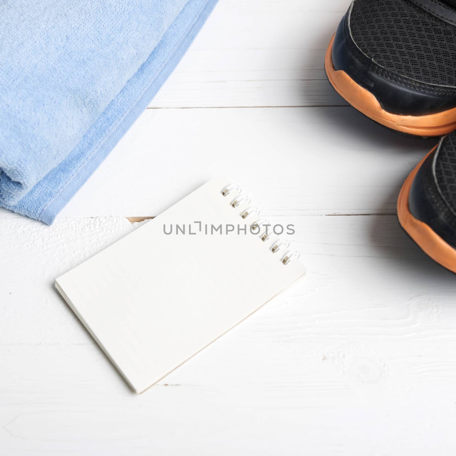 fitness equipment : running shoes,blue towel and notepad on white wood table