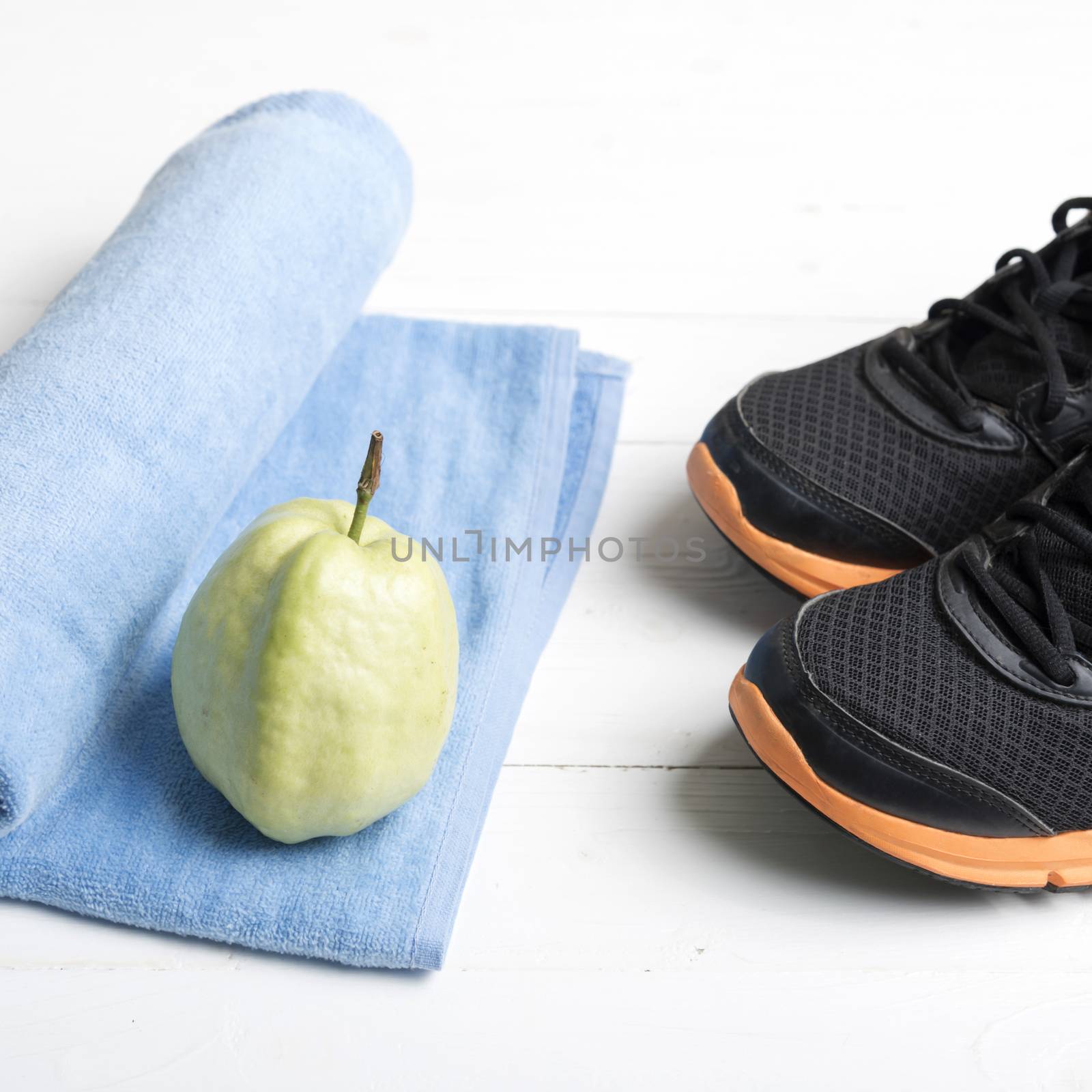 fitness equipment : running shoes,blue towel and guava fruit on white wood table