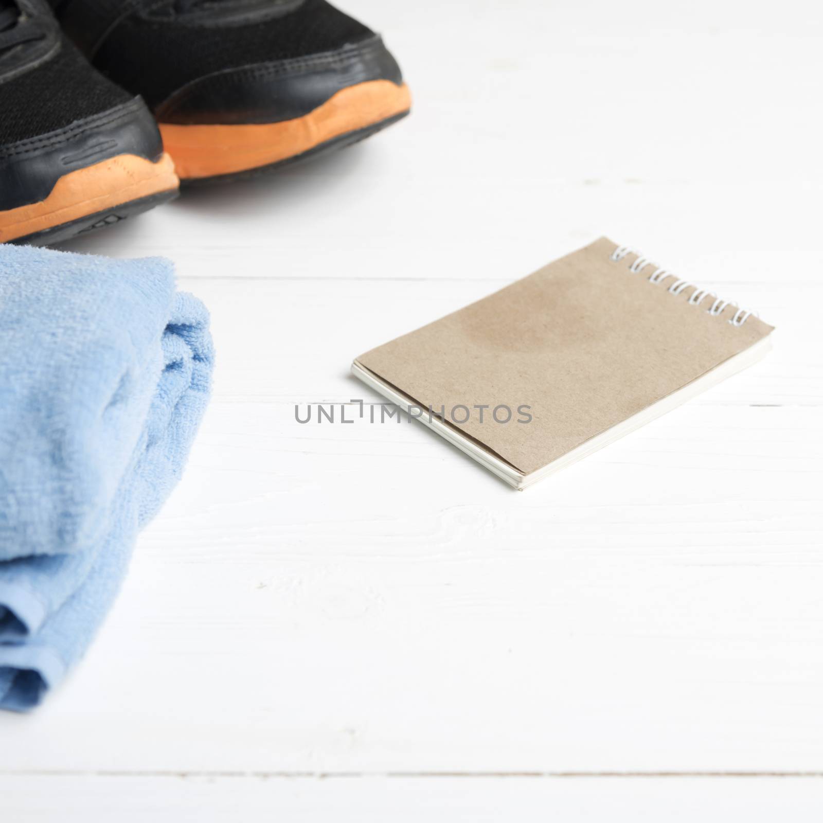 fitness equipment : running shoes,blue towel and notepad on white wood table