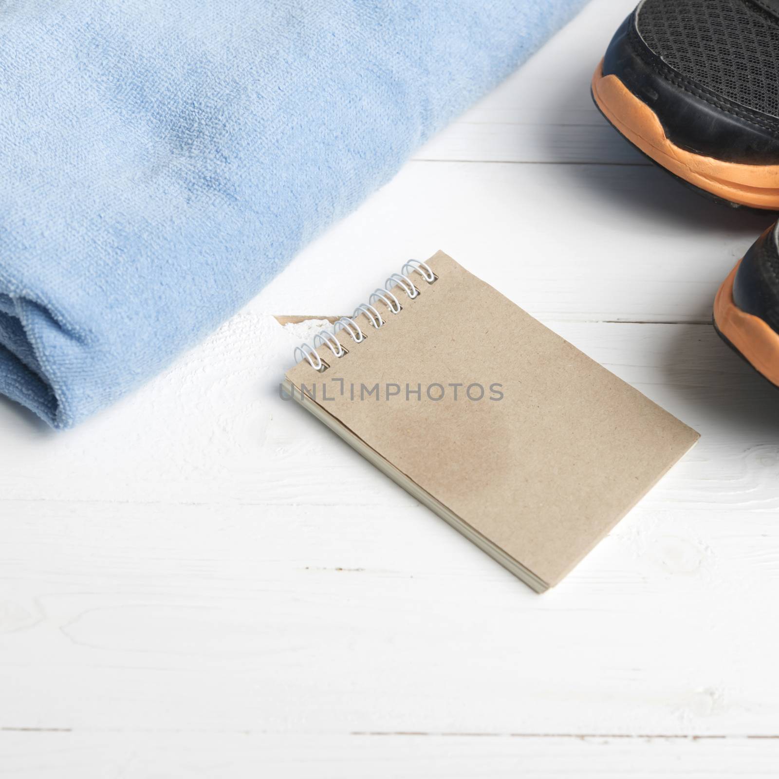 fitness equipment : running shoes,blue towel and notepad on white wood table
