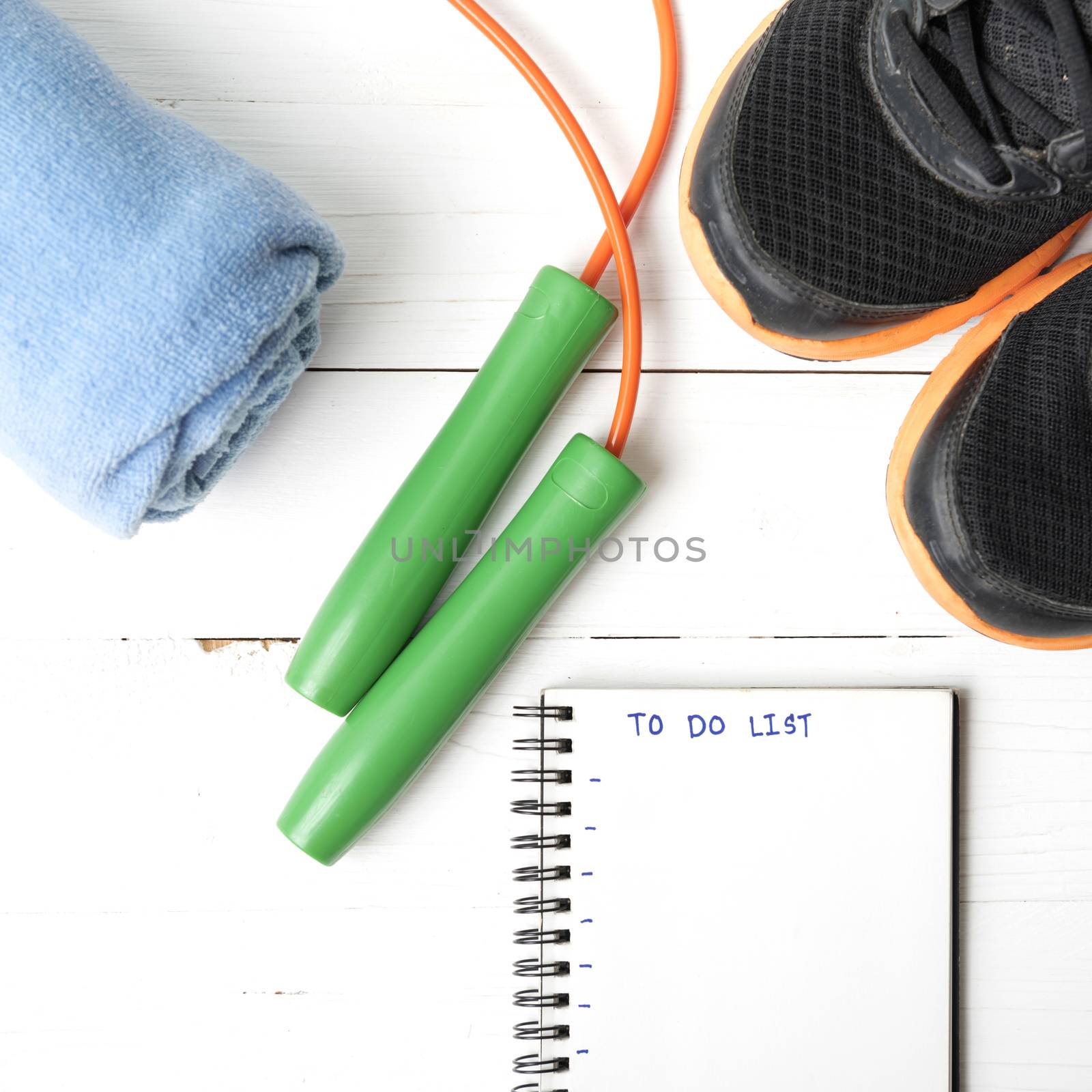 fitness equipment : running shoes,towel,jumping rope and notebook write to do list on white wood table