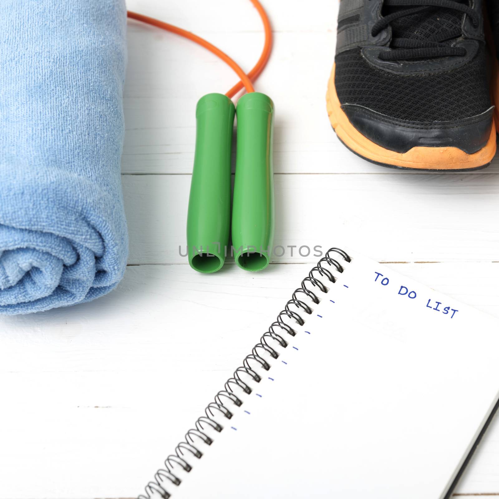 fitness equipment : running shoes,towel,jumping rope and notebook write to do list on white wood table